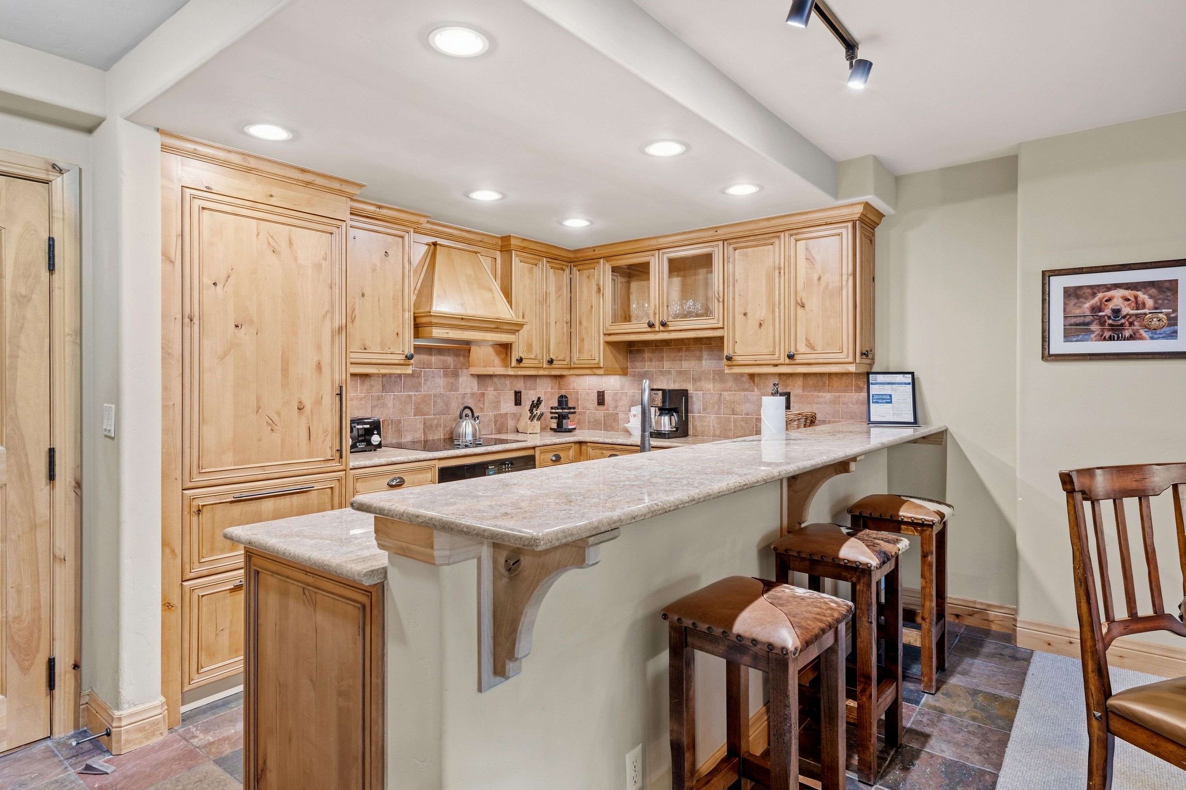 A kitchen with wooden cabinets, a marble countertop, and a bar area with stools.