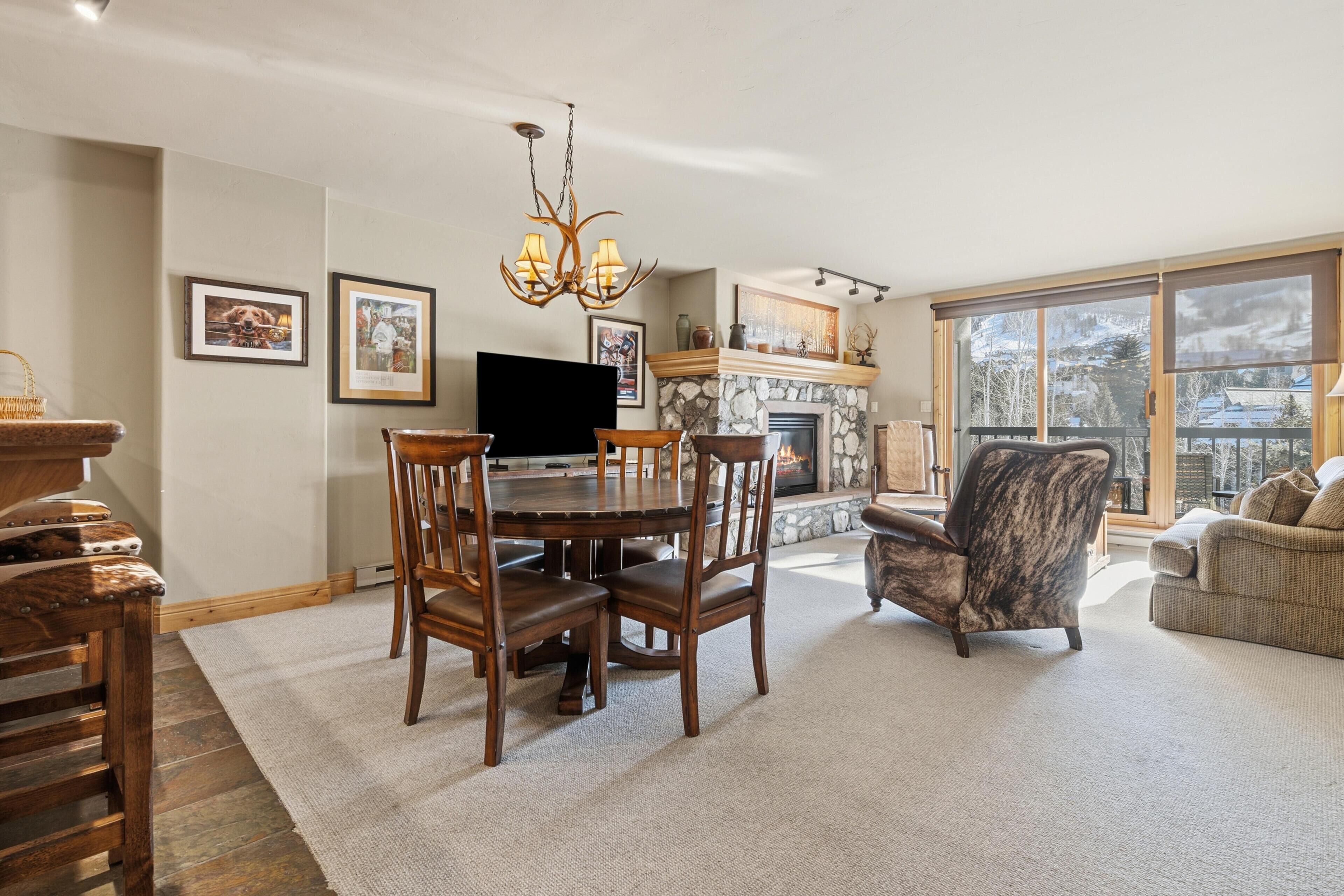 A dining area with a stone fireplace, a chandelier, and a large window with a view.