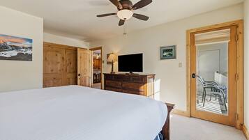 Un dormitorio con cama, ventilador de techo, televisor, muebles de madera y una puerta que da a un espacio exterior.