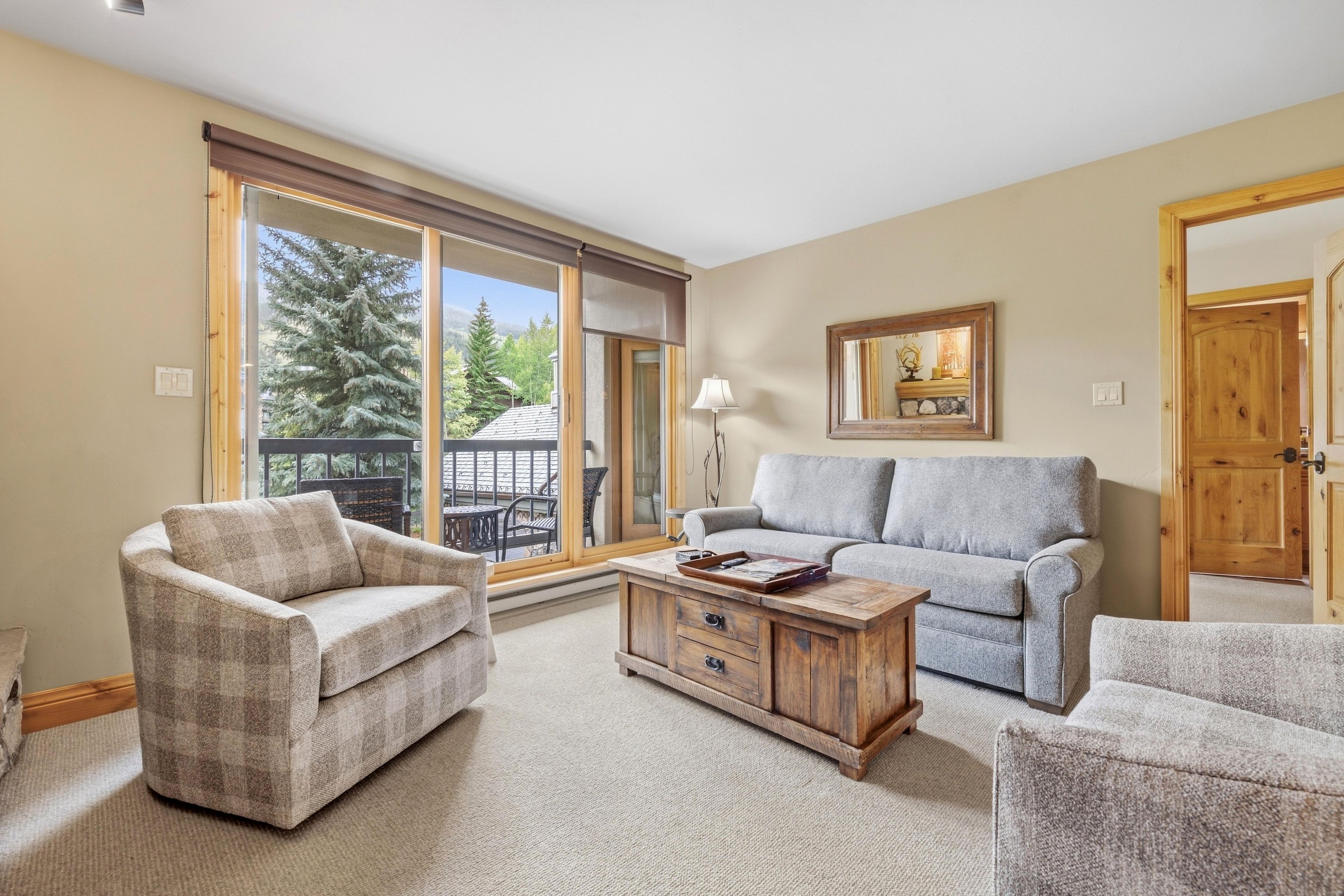 A living room with a sofa, armchair, and coffee table, a sliding glass door to a balcony, and a wooden door.