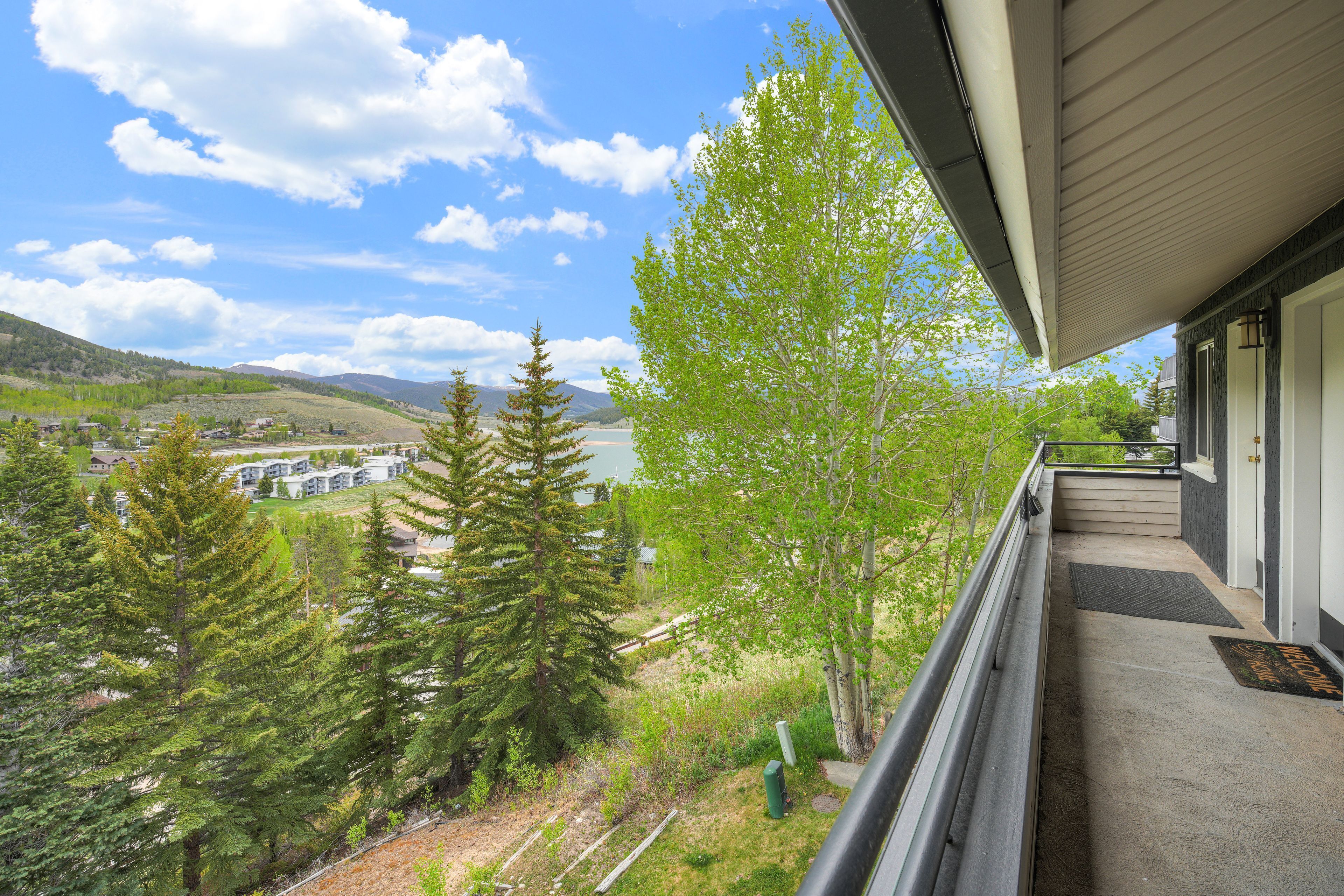 A balcony with a view of a residential area, trees, and a distant body of water.