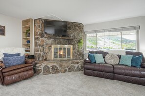 Ein Wohnzimmer mit Kamin aus Stein, Ledersofas und einem großen Fenster mit Blick.