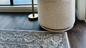 Ein Zimmer mit einem großen Fenster, einem runden Sessel, einem kleinen Tisch und einem gemusterten Teppich.