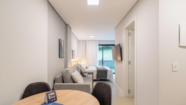 A modern hotel room with a dining area, a sofa, a TV, and a balcony with a view. - Studio in Center of Rosa, Rooftop w/ Pool Rso0003 (Imbituba)