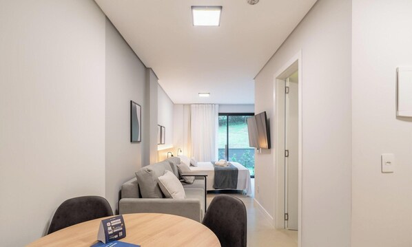 A modern hotel room with a dining area, a sofa, a TV, and a balcony with a view. - Studio in Center of Rosa, Rooftop w/ Pool Rso0003 (Imbituba)