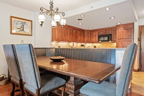 A dining area with a wooden table and chairs, a chandelier, and wooden cabinets in the background. - Borders Lodge L303 2BD Beaver Creek Ski-in, Ski-out Condo (Avon)