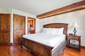A bedroom with a wooden bed, a nightstand, a lamp, and wooden doors. - Borders Lodge L303 2BD Beaver Creek Ski-in, Ski-out Condo (Avon)