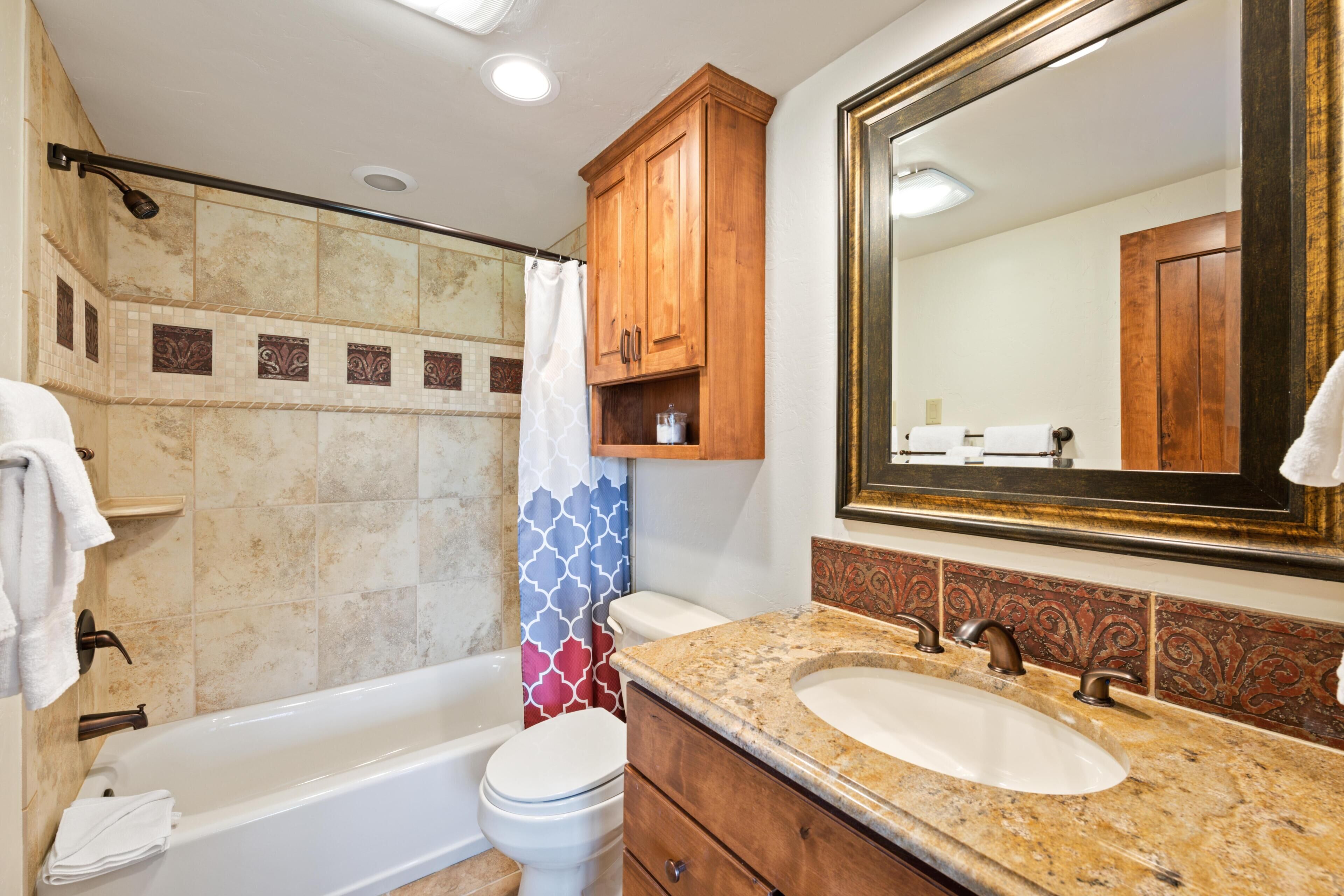 A bathroom with a bathtub, toilet, vanity with a sink, and a large mirror.