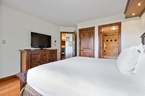 A bedroom with a large bed, a wooden dresser, a television, and a bathroom visible through an open door. - Borders Lodge L303 2BD Beaver Creek Ski-in, Ski-out Condo (Avon)