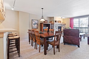 A dining area with a wooden table and chairs, a fireplace, and a large window with a view. - Borders Lodge L304 2BD Beaver Creek Ski-in, Ski-out Condo (Avon)