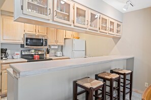 A kitchen with wooden cabinets, a microwave, a refrigerator, a coffee maker, and a bar stool. - Borders Lodge L304 2BD Beaver Creek Ski-in, Ski-out Condo (Avon)