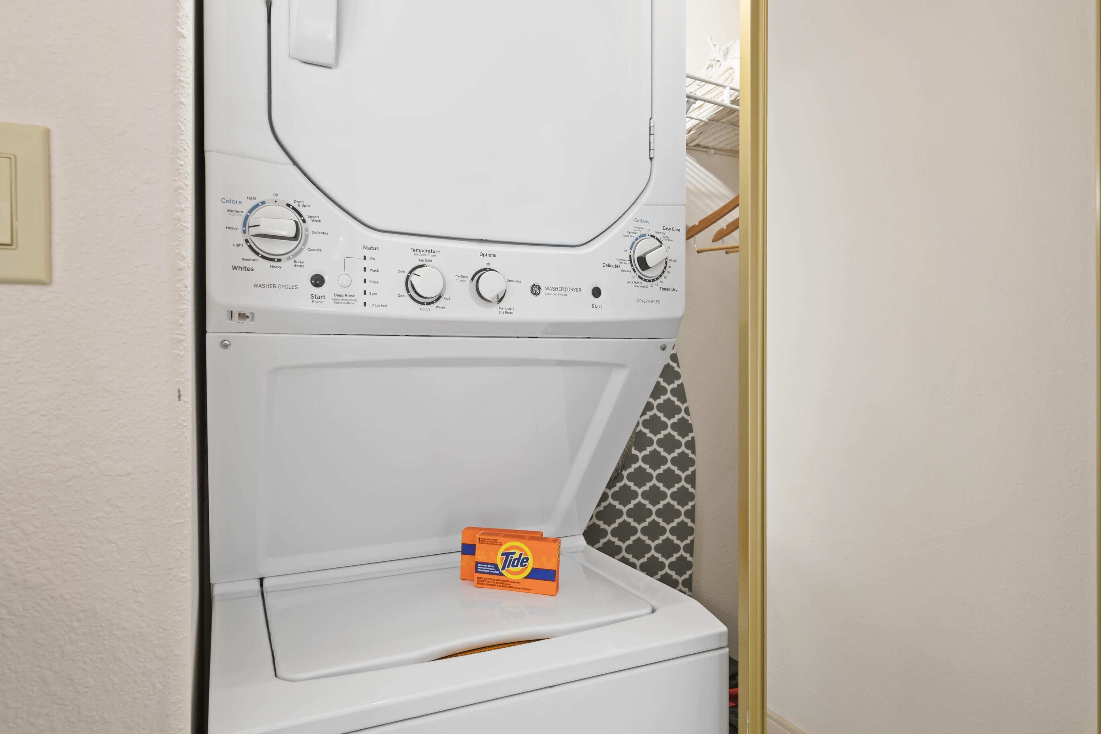 Una lavadora de carga frontal con detergente Tide, perillas de control y una pared con diseño.