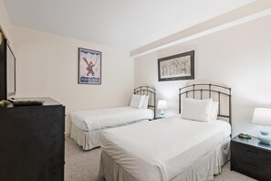 Habitación de hotel con dos camas, un escritorio, un aparador, un cuadro enmarcado y un cartel en la pared.