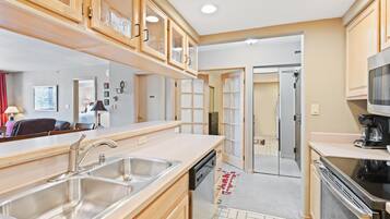 Una cocina compacta con armarios de madera, un lavamanos de acero inoxidable, un lavavajillas y un microondas.