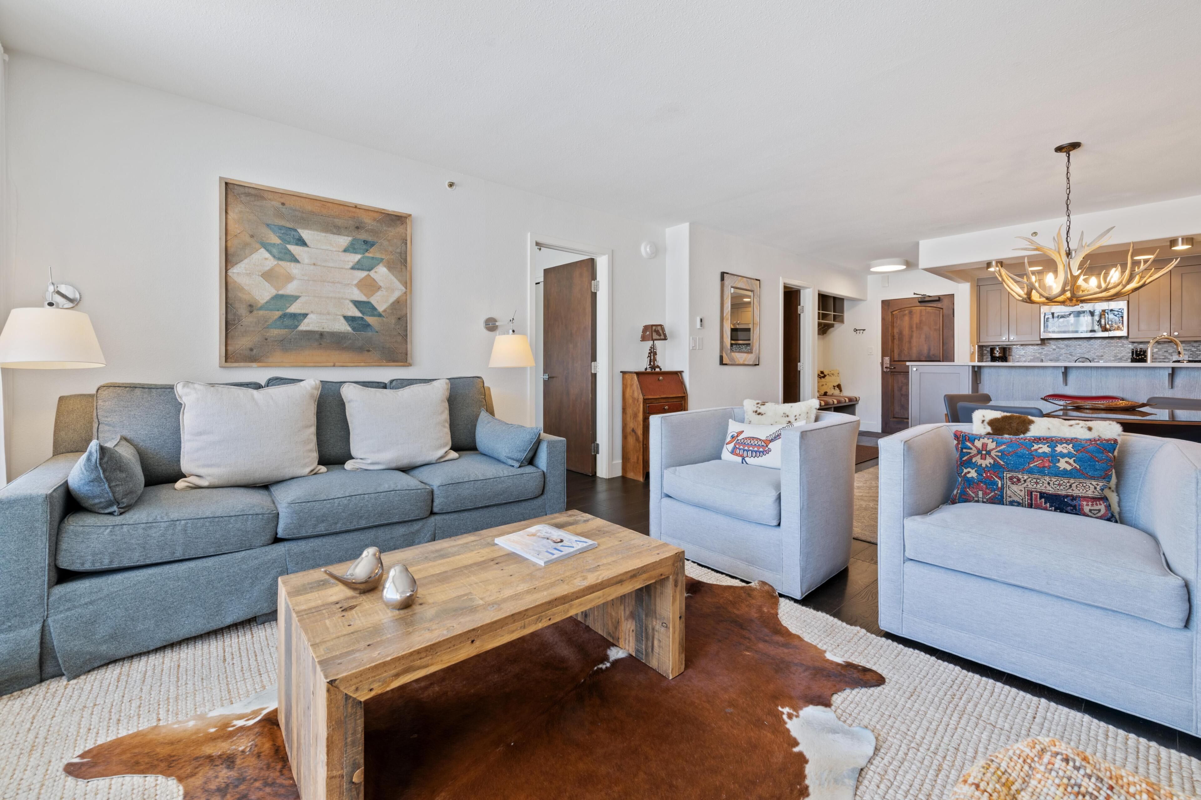 Ein modernes Wohnzimmer mit Sofa, Sessel, Couchtisch und einem Kuhfellteppich.