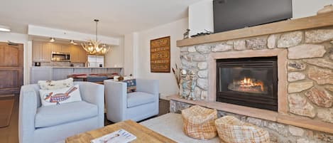 Una sala de estar moderna con chimenea, una cocina al fondo y un área de descanso con una mesa de centro.