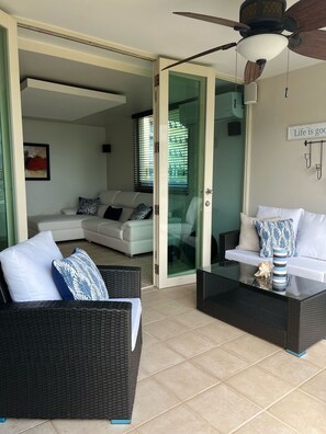 A modern living room with a glass door leading to another room, a ceiling fan, and a sign on the wall. - Caribbean Ocean View 3-BR Villa with Panoramic Ocean Views & 2 Private Terraces (Humacao)