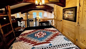 Ein Holzhütten-Zimmer mit einem Bett, einer Chandelüster, einem Esstisch und Blick ins Freie.