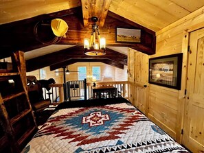 A wooden cabin room with a bed, a chandelier, a dining table, and a view of the outside. - Secluded NC Mtn Red Barn Cabin • 3 Acres • Near Ocoee Rafting, Lakes, Casino (Murphy)