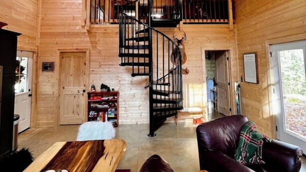 Ein Holzblockhaus-Interieur mit Wendeltreppe, Ledersofa und Esstisch.
