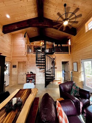 A wooden cabin interior with a spiral staircase, a leather sofa, and a dining table.