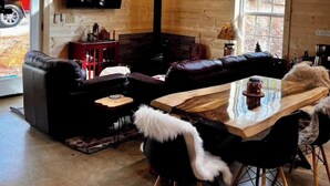 Ein Blockhaus-Interieur mit Kamin, Ledersofa, Esstisch aus Holz und einem an der Wand befestigten Fernseher.