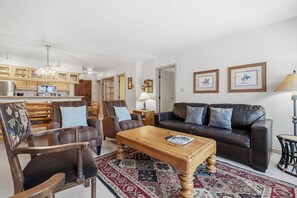 A living room with a sofa, chairs, a coffee table, and a rug. There is a kitchen area with cabinets and a refrigerator. - Borders Lodge L306 2BD Beaver Creek Ski-in, Ski-out Condo (Avon)