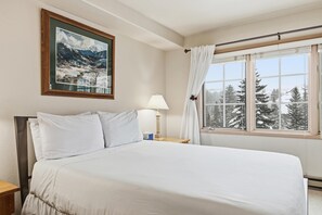 A neatly made bed with white linens, a framed landscape painting above it, a bedside lamp, and a window with curtains. - Borders Lodge L306 2BD Beaver Creek Ski-in, Ski-out Condo (Avon)