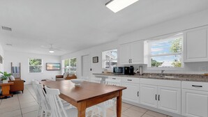 Una cocina moderna con armarios blancos, una mesa de comedor de madera y un ventanal con persianas.