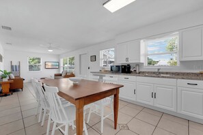 Eine moderne Küche mit weißen Schränken, einem Holztisch und einem großen Fenster mit Jalousien.