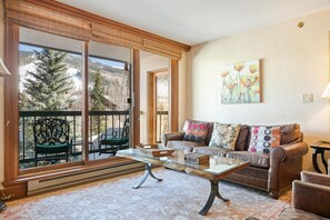 A living room with a glass coffee table, leather sofa, and a painting on the wall. - Borders Lodge L308 2BD Beaver Creek Ski-in, Ski-out Condo (Avon)