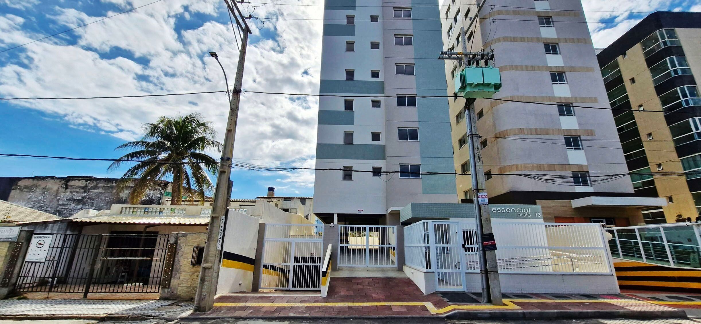 Un edificio de varios pisos con entrada porticada, una palmera y un farol.