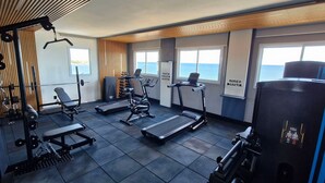 A gym with various exercise equipment, a treadmill, and a view of the sea through large windows. - COPIA0106 - Edifício Essencial Piata (Salvador)