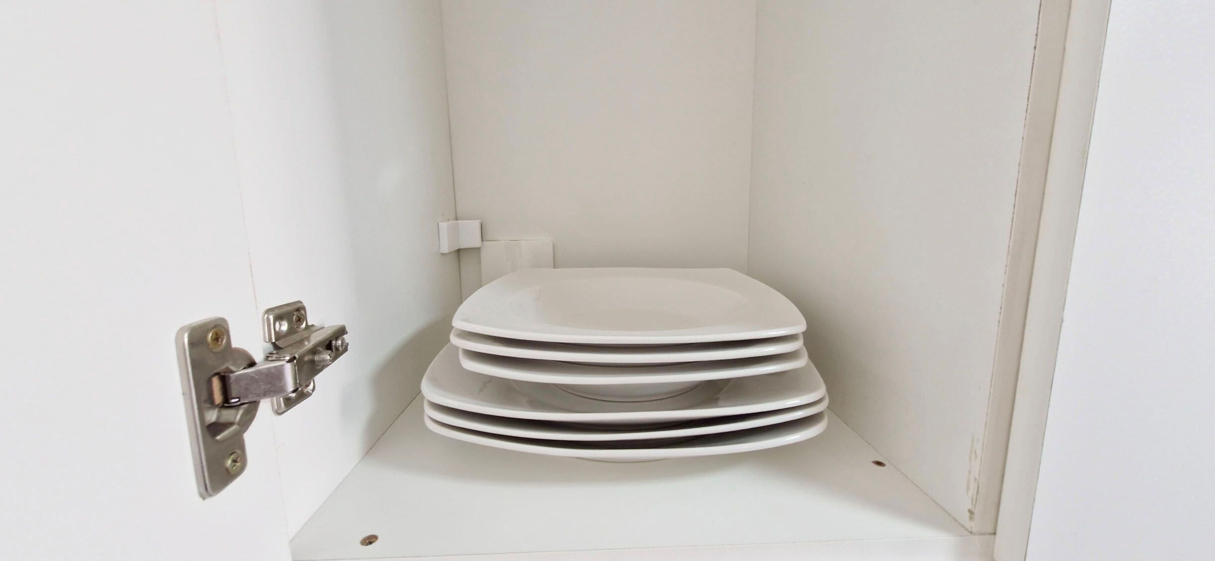 A white toilet stall with a stack of white plates on the floor.