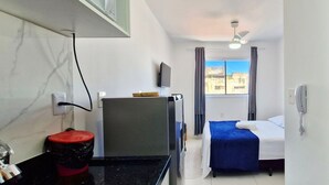 A hotel room with a bed, a TV, a desk, a trash bin, and a window with curtains. - COPIA0106 - Edifício Essencial Piata (Salvador)