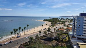 A coastal road with a beach, palm trees, and a cityscape in the background. - COPIA0106 - Edifício Essencial Piata (Salvador)