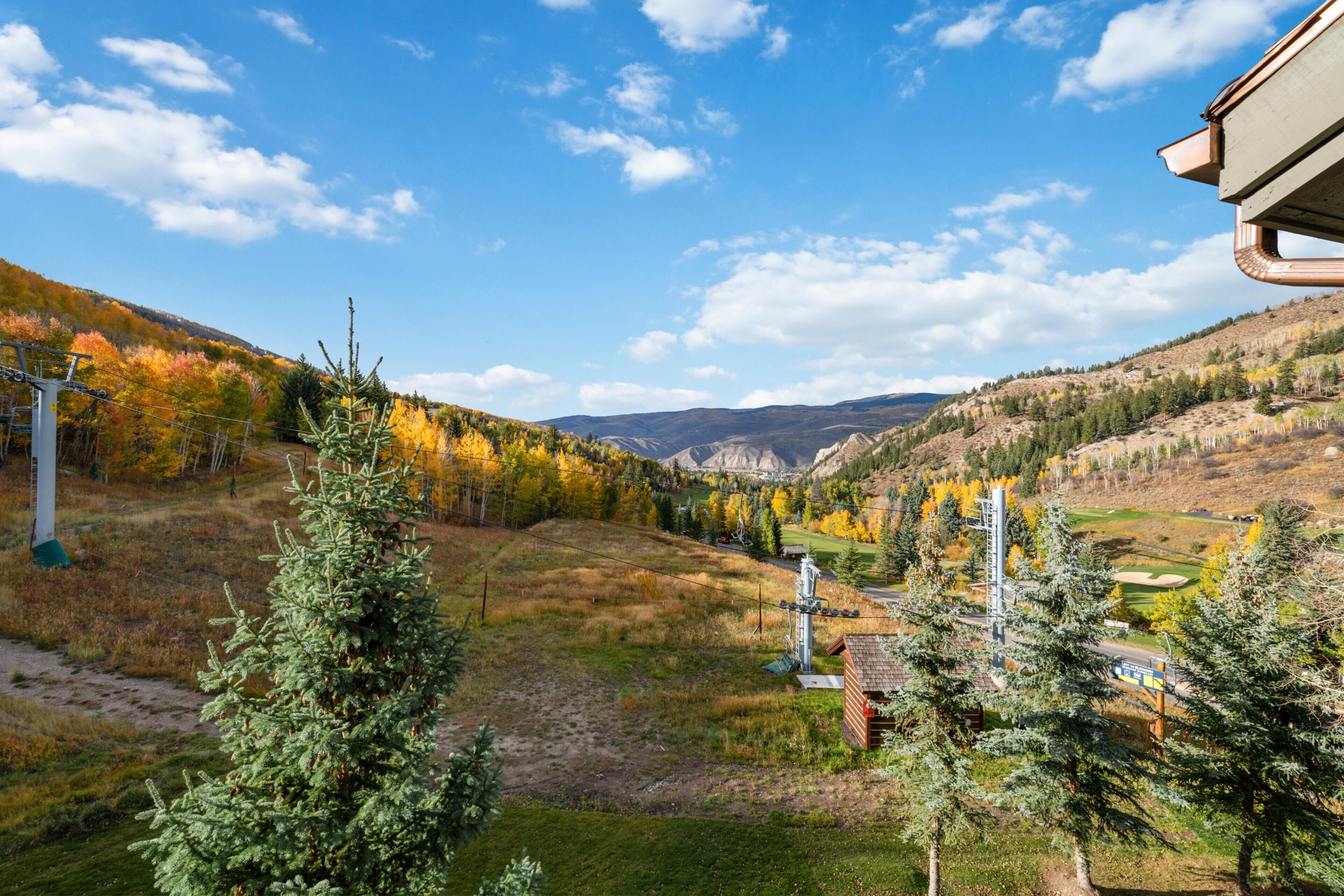 A mountainous landscape with autumn foliage, a ski lift, and a small cabin.