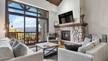 A cozy living room with a stone fireplace, comfortable seating, and a large sliding glass door leading to a balcony.