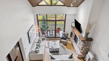 A spacious living room with a stone fireplace, a large window overlooking a deck, and a modern sofa set.