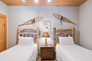 Une chambre avec deux lits en bois, une table de chevet avec une lampe et un panneau encadré accroché au mur.
