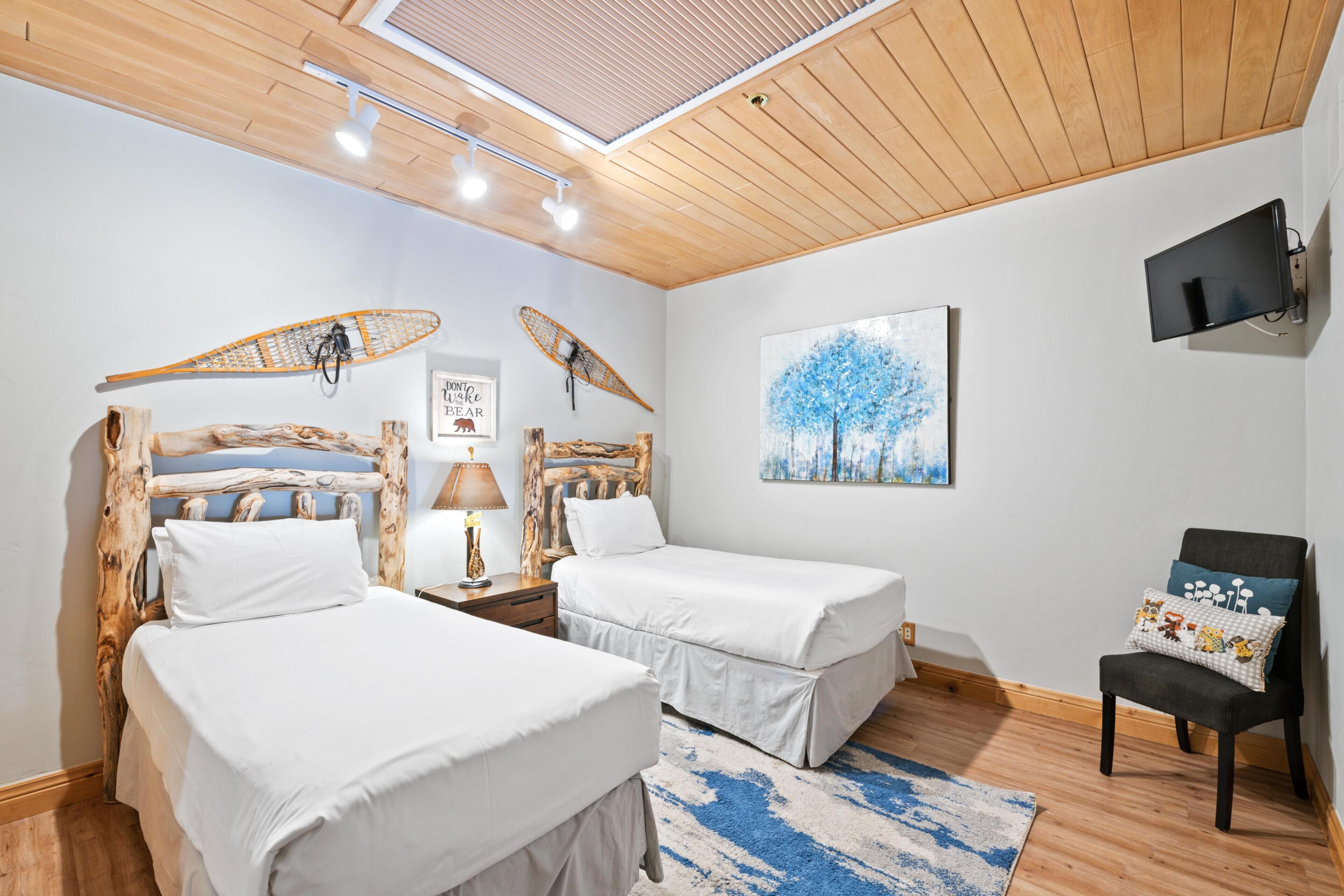 Quarto com duas camas, uma TV, uma cadeira e um quadro.