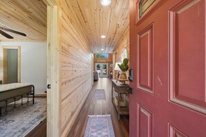A wooden interior hallway with a bed, a red door, and a view into another room. - Sleeps 7, Waterfront, Dock, Great Water, Paddleboard, Firepit + More! (Sparta)