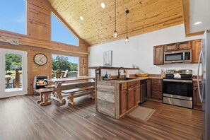 A spacious kitchen with wooden cabinetry, a large island, and a view of the outdoors. - Sleeps 7, Waterfront, Dock, Great Water, Paddleboard, Firepit + More! (Sparta)