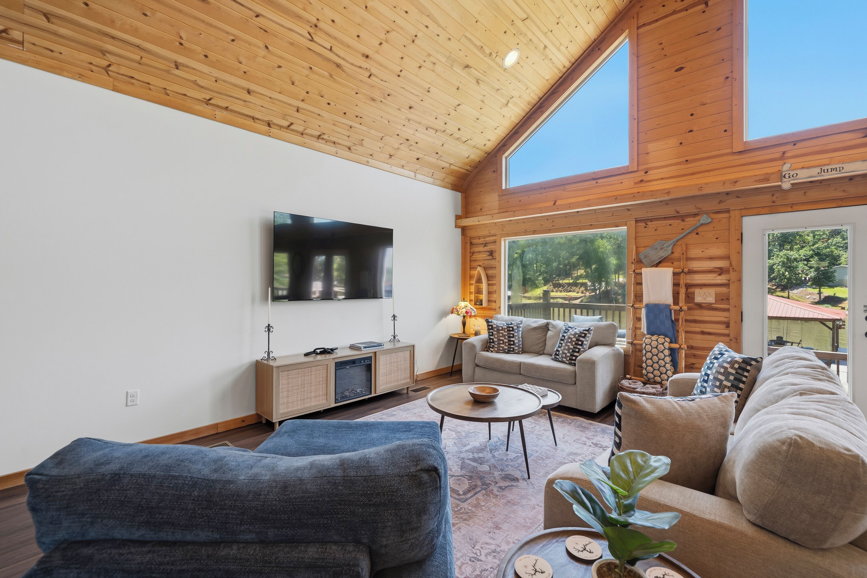 Un salon moderne avec un plafond en bois, un téléviseur à écran plat, un ensemble de canapés, une table basse et une vue sur l’extérieur.