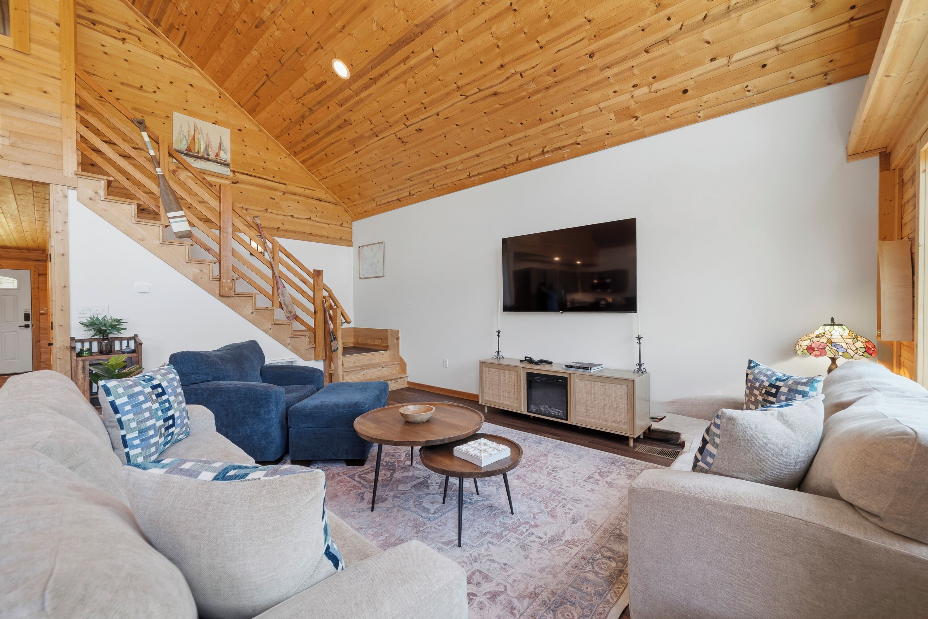A living room with a staircase, sofas, a TV, and a wooden ceiling.