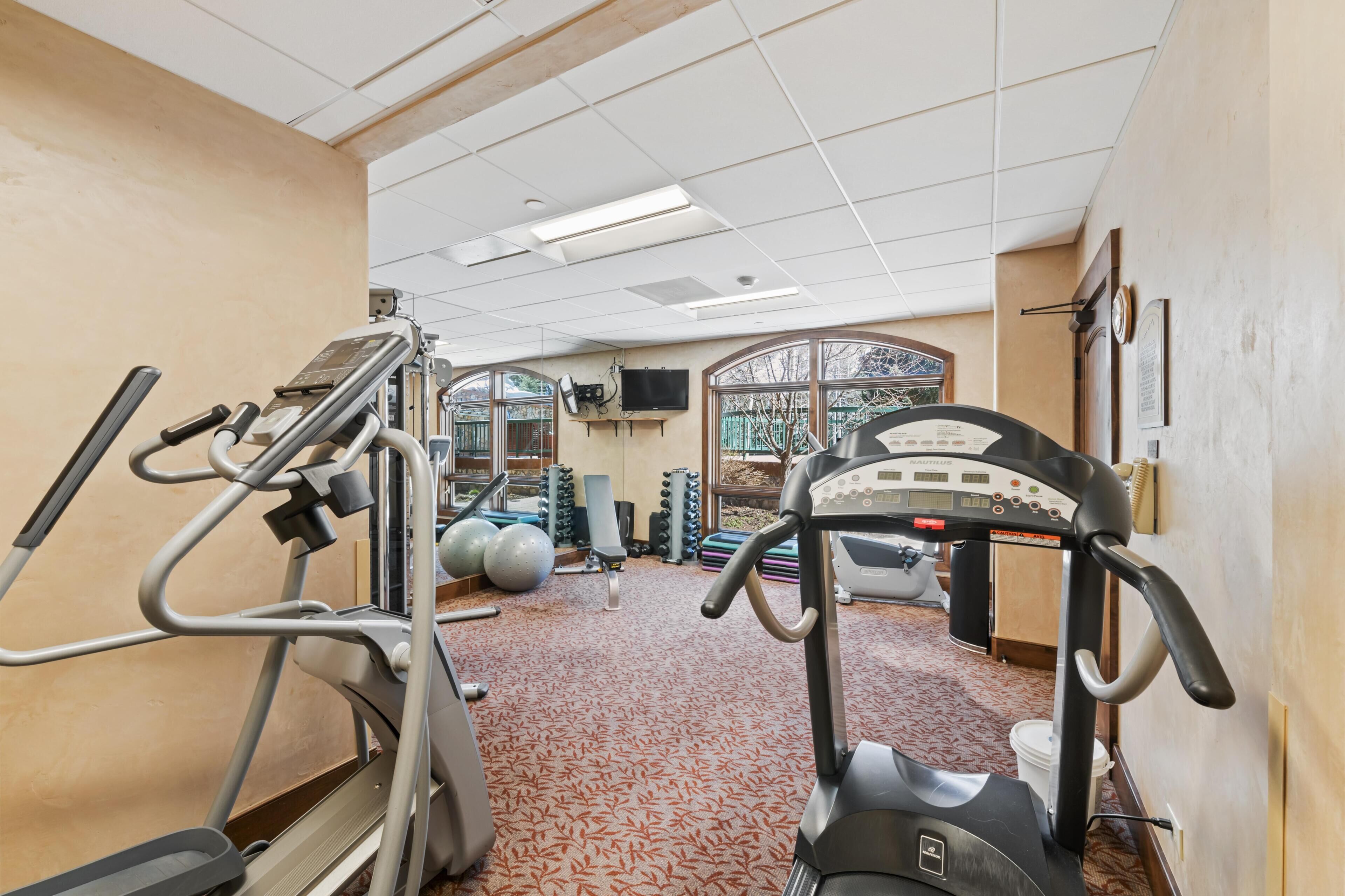 A gym with exercise equipment, a patterned carpet, and a window with a view.