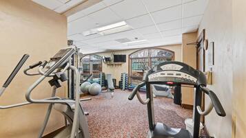 A gym with exercise equipment, a patterned carpet, and a window with a view.