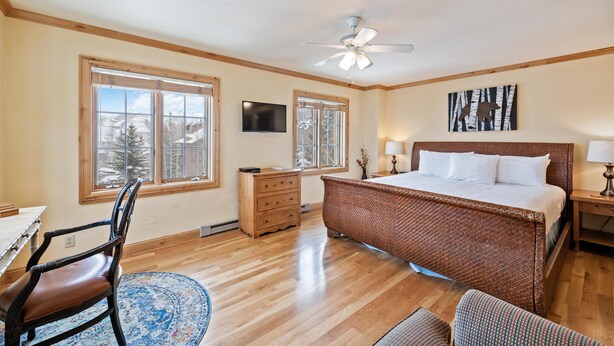 A bedroom with a large bed, wooden floor, a ceiling fan, and a window with a view of trees. - Borders Lodge L400 Hotel Room Beaver Creek Ski-in, Ski-out Condo (Avon)