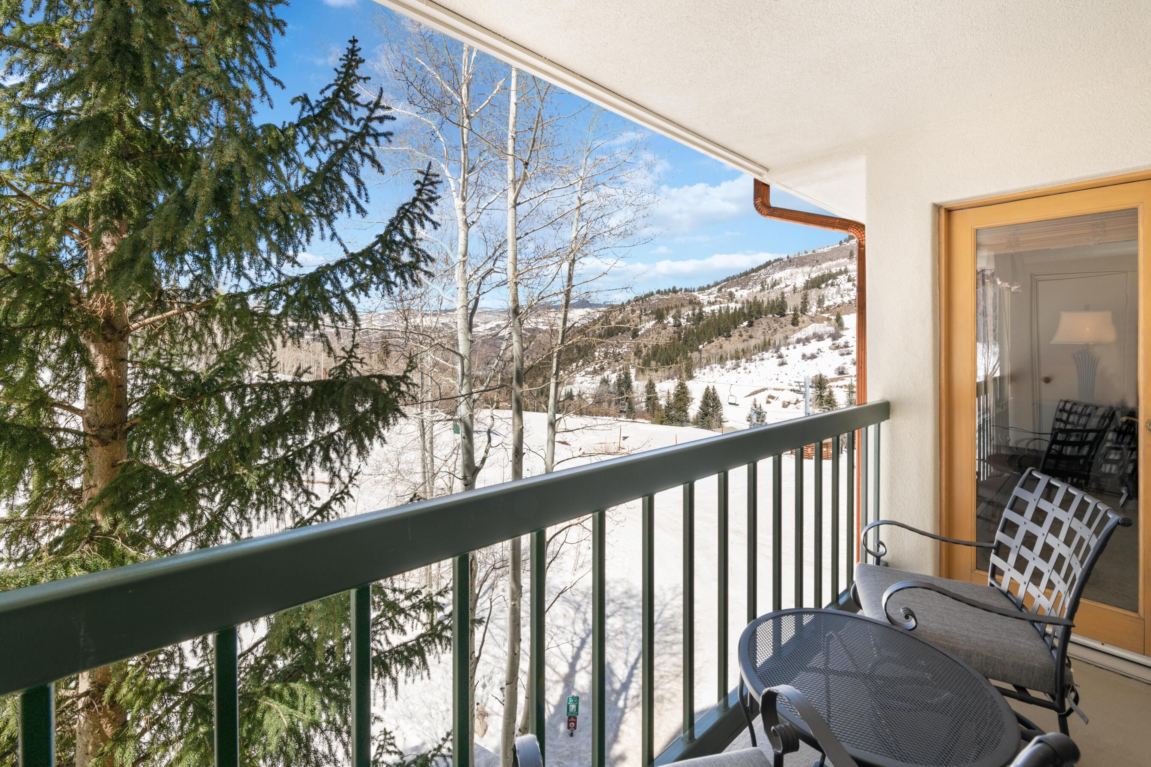 A balcony with a view of a snowy landscape, a chair, and a table.