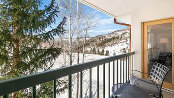 A balcony with a view of a snowy landscape, a chair, and a table.